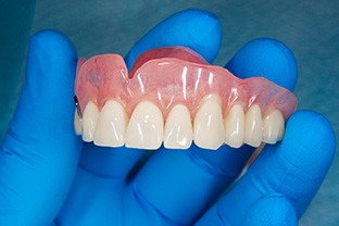 Gloved hand holding full dentures