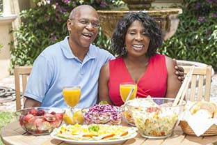 senior man and woman sitting at a table with various foods and beverages