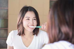 woman brushing her teeth in front of a mirror