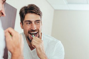 Man in white shirt smiling while brushing his teeth