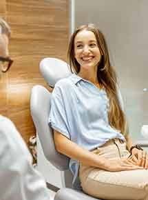 A young woman sitting in a chair and speaking to her dentist