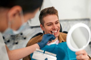 Man smiling at reflection while selecting shade of veneer