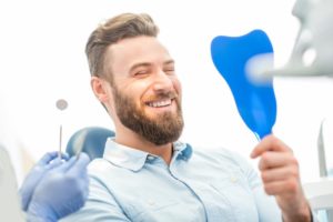 a man looking in a mirror with a bright beautiful smile from cosmetic dental treatments