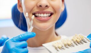 Nose-to-shoulder view of woman in dental chair smiling with shade guide held to her teeth